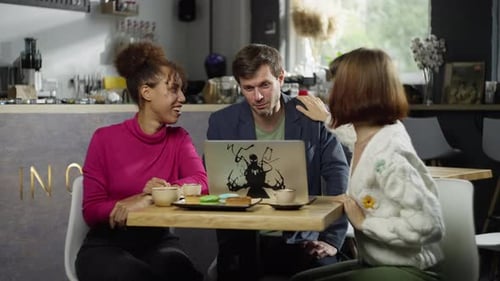 Friends Look at Photos Together on a Computer in a Cafe Smile and Have Fun