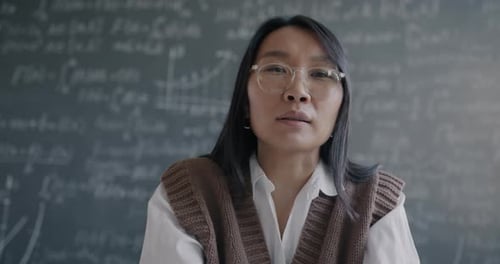 Woman Speaking in Front of Chalkboard Filled with Formulas