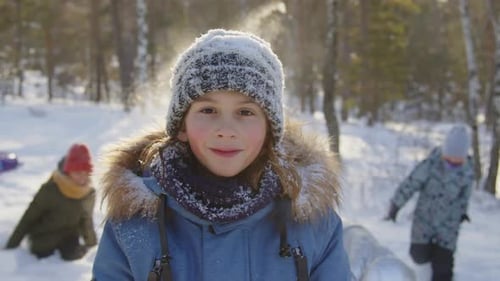 Porträt eines glücklichen, schneebedeckten Jungen, der im verschneiten Wald posiert