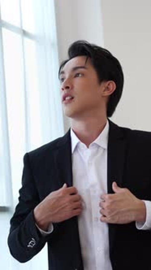 Handsome Man Buttons Shirt Before a Window