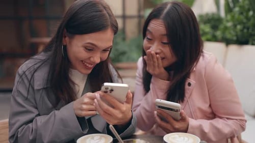 Diverse Female Friends Enjoying Photos on Smartphone at Cafe