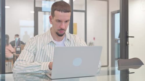 Young Adult Focused on Laptop in Office Setting