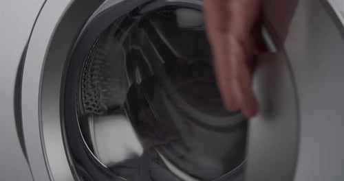 Young man adding laundry detergent to machine load pre-wash