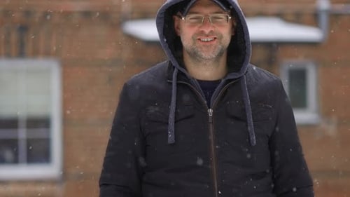 Smiling Man in Hooded Jacket During Snowfall