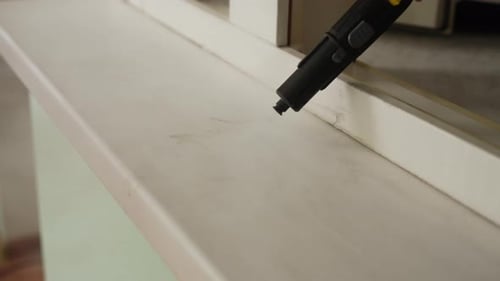 Haushälterin verwendet Dampfreiniger, um Fensterbank beim Frühjahrsputz effektiv zu reinigen Erstellen