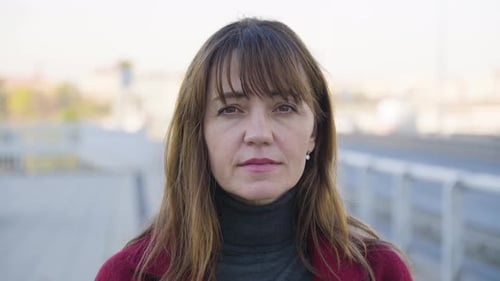 An Attractive Middleaged Caucasian Woman Looks Seriously at the Camera By a Busy Road