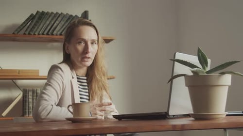 Une jolie femme parle assise à une table devant un ordinateur portable et gescule activement avec