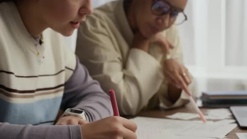 Teen Student Taking Notes while Tutor Sitting Near Her