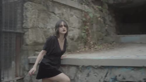 Pale girl with expressive make-up and black dress runs closed in a cell with bars and stretches her