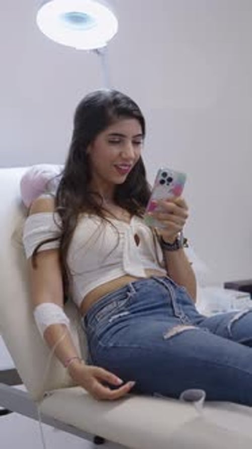 Schöne Frau sitzt auf einem Kliniktisch und hat Spaß mit dem Telefon
