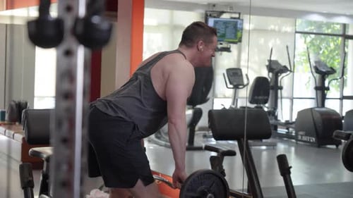 A man performing a barbell bent-over row in a gym. Focused on back and arm strength.