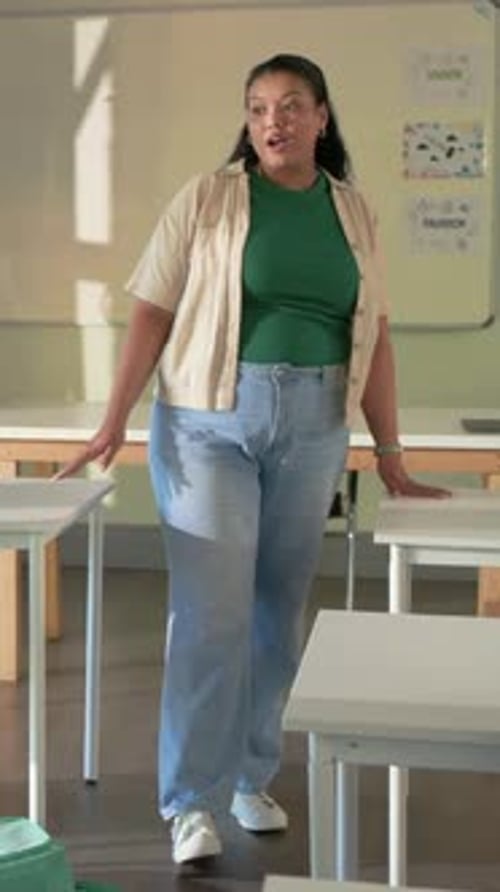 Vertical video: Entering woman teacher in green top moving through class, teaching near whiteboard
