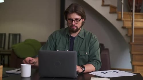 Young Businessman Working with Laptop and Drinking Coffee Sitting at Table in Home Office Spbas
