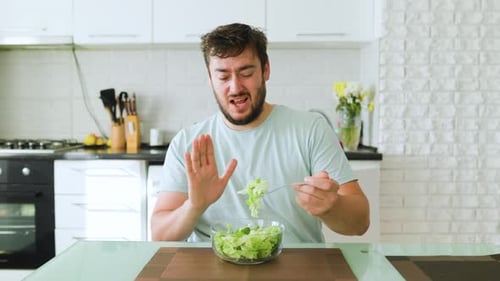 A Young Man Holds a Fork with a Salad with One Hand the Other Shows a Stop Diet