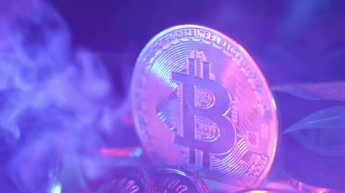 close-up shot of a shiny golden Bitcoin under led lights with smoke passing