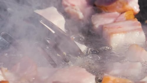 Sausages and meat sizzling in a hot wok. Close-up shot of the cooking process with steam rising.