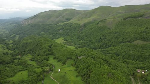 Flying over beautiful green mountains. Panorama of mountains and alpine houses below. Aerial view.