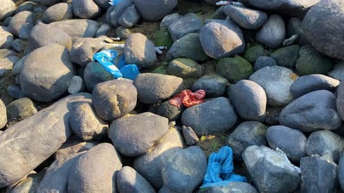 Rocky river bank covered in trash, a stark reminder of an environmental issue. Pollution, waste, and