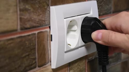 Sideways view of a dual power outlet. Connecting and disconnecting a black power plug by a woman's h