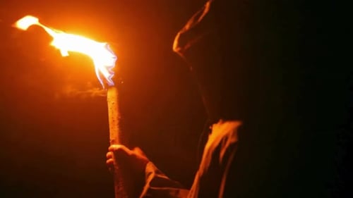 Hooded Figure Holding a Burning Torch in Darkness