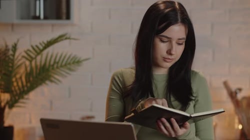Young Woman Writing in Notebook with Laptop