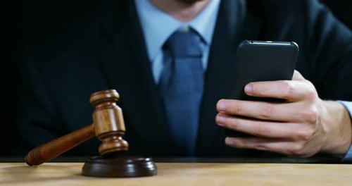 Man Holds Phone Next to Gavel on Desk
