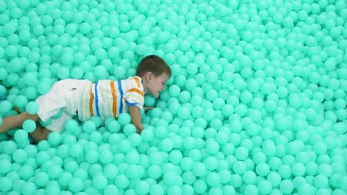 Un garçon joyeux joue dans une piscine avec beaucoup de balles dans la salle de jeux