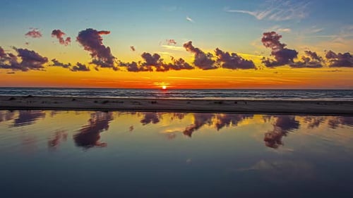 The canal water reflects a colorful sunset over a seashore beach - golden time lapse