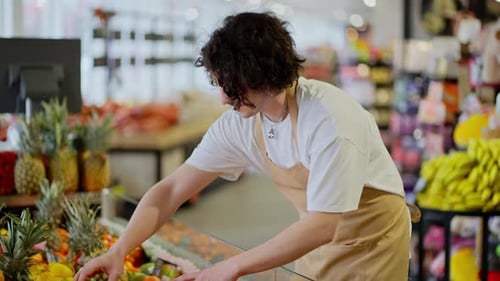 A Confident Guy a Brunette Store Worker with Curly Hair in a White Tshirt and a Yellow Apron Lays