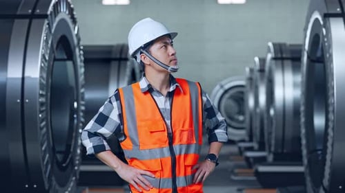 Asian Male Engineer Looking Around While Standing With Arms Akimbo In Metal Factory