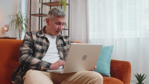 Man Sits on Couch Using Laptop with Expression of Joy