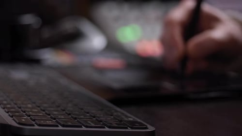 Hand working with tablet, keyboard from a side perspective with blurred background.