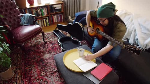 Young Man Plays Guitar and Writes Song at Home