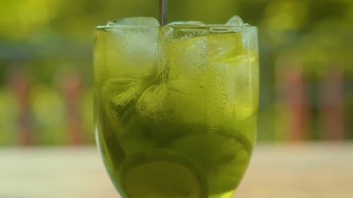 Stirring Lemonade in Glass Tropical Background Close Up Limes Spinning