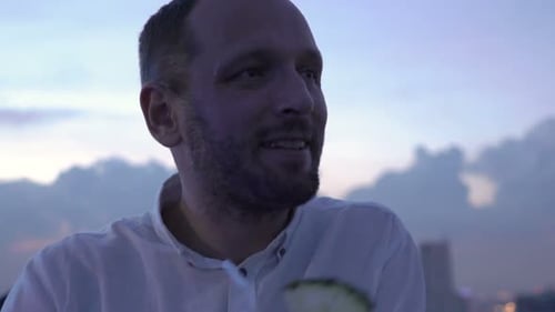 Young man enjoying a cocktail on a luxury rooftop bar terrace at dusk