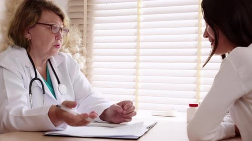 Senior woman doctor consults with young patient in modern medical office.