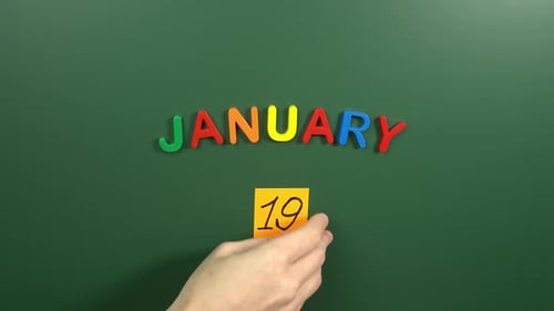 Hand sticking a sticker 19 January calendar day on school board. 19 date of January. Nineteenth day