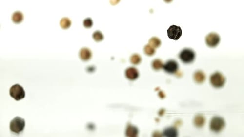 Falling multicolored peppercorns creating splash against white background