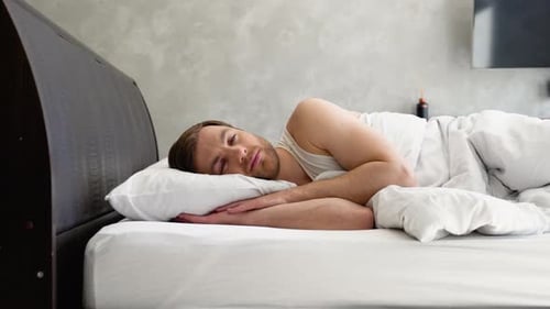 Young Man Lies Down in Bed Under the Covers and Falls Asleep at Home Relaxation Concept