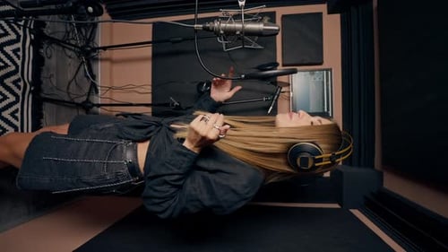 girl singer singing in a recording studio with headphones in front of microphone to create a song