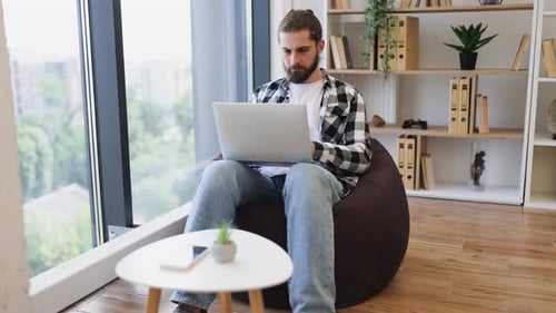 Young Man Working on Laptop in Cozy Home Office with Natural Light