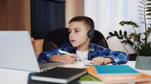 Clever School Boy with Headset Having Video Call on Laptop with Tutor at Home