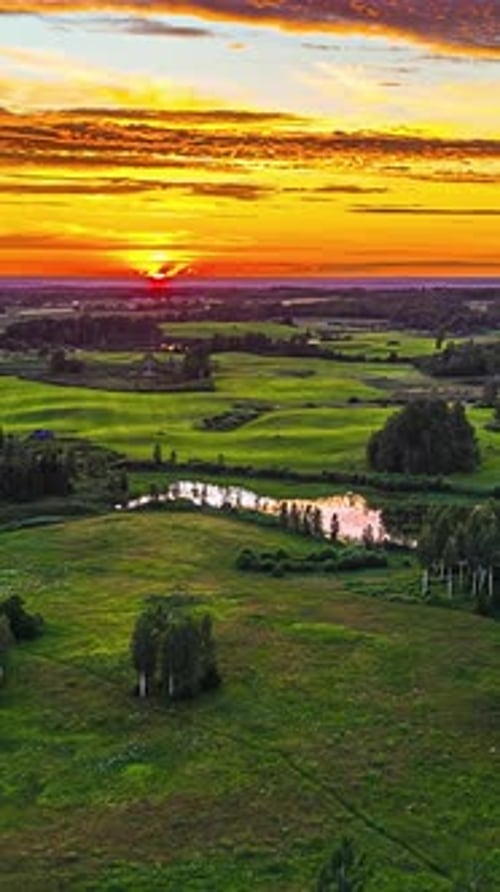 Vibrant sunset over lush green fields with reflective ponds in cinematic hyperlapse
