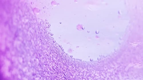 Makroaufnahme von vielen kleinen violetten Blasen, die im Wasser vor hellem Hintergrund funkeln