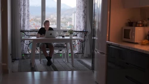 Young Adult Using Laptop in Apartment with City View