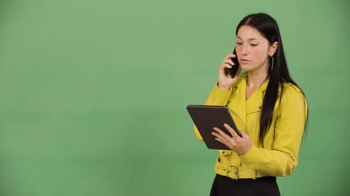 A Young Beautiful Caucasian Woman Talks on a Smartphone and Looks at a Tablet Green Screen Studio