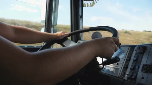 Close Up Male Arms of Lorry Driver Holds a Big Steering Wheel While Operating a Truck at Sunny Day