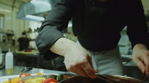 Chef Putting Vegetables on Plate with Fish in Restaurant Kitchen