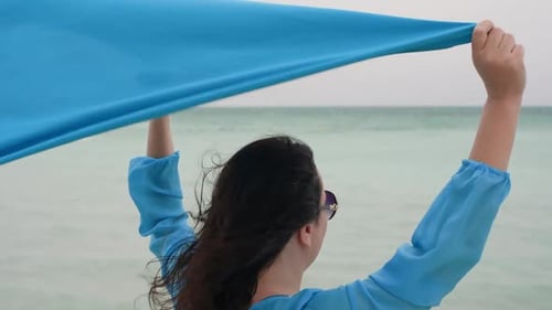 Tourist Waving Blue Scarf While Standing at Beach