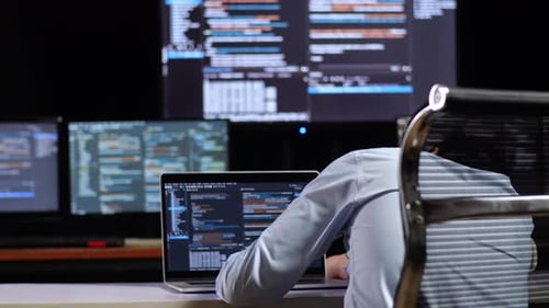 Programmeur s'appuyant sur une table tout en écrivant du code par un ordinateur portable utilisant plusieurs moniteurs affichant la base de données